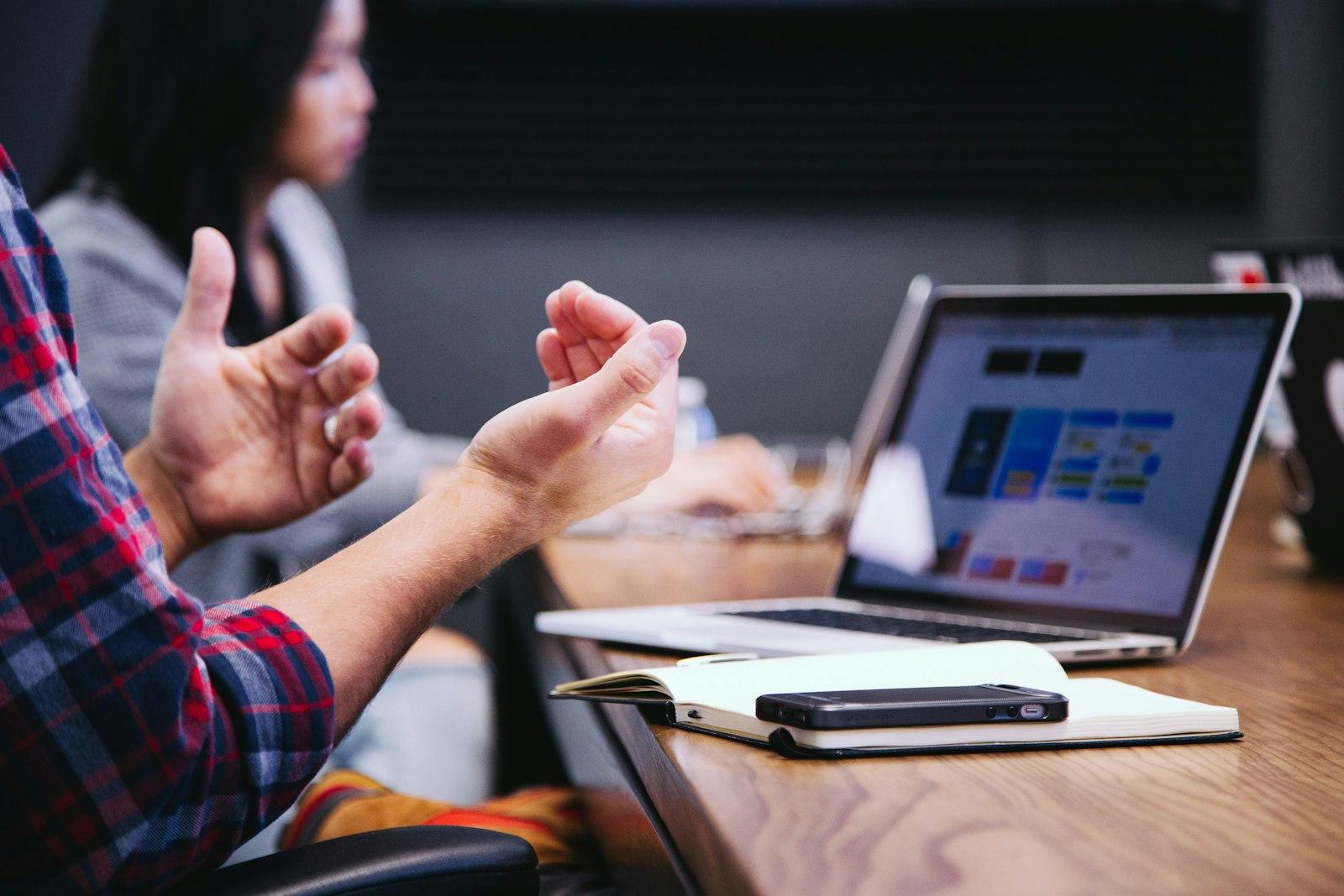 A conversation across a laptop, one person explaining with their hands